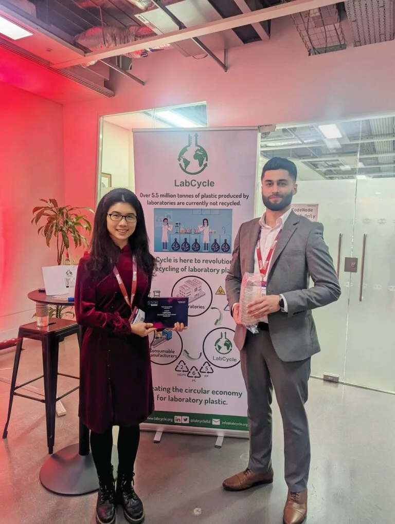 Two members of the LabCycle team holding the award plaque and recycled consumables at the LabCycle stand